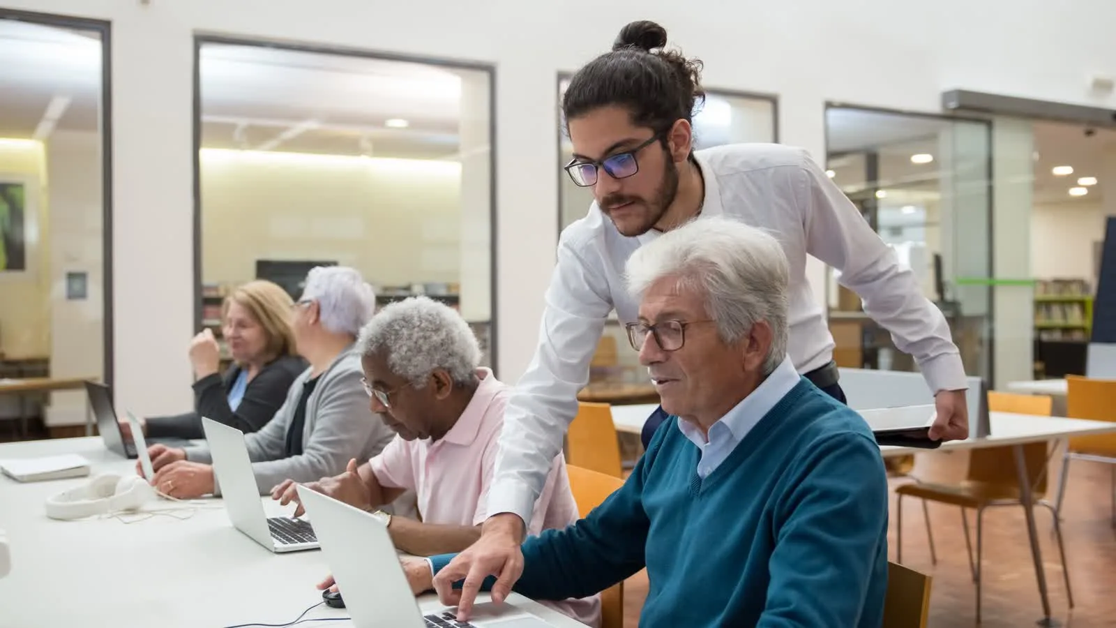 Formatore assiste adulti durante una lezione al computer in biblioteca